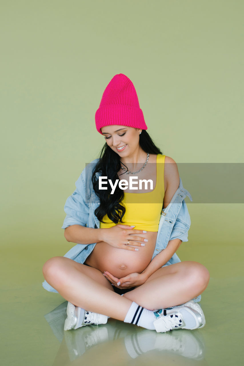 Stylish young expectant mother in stylish clothes on an olive background