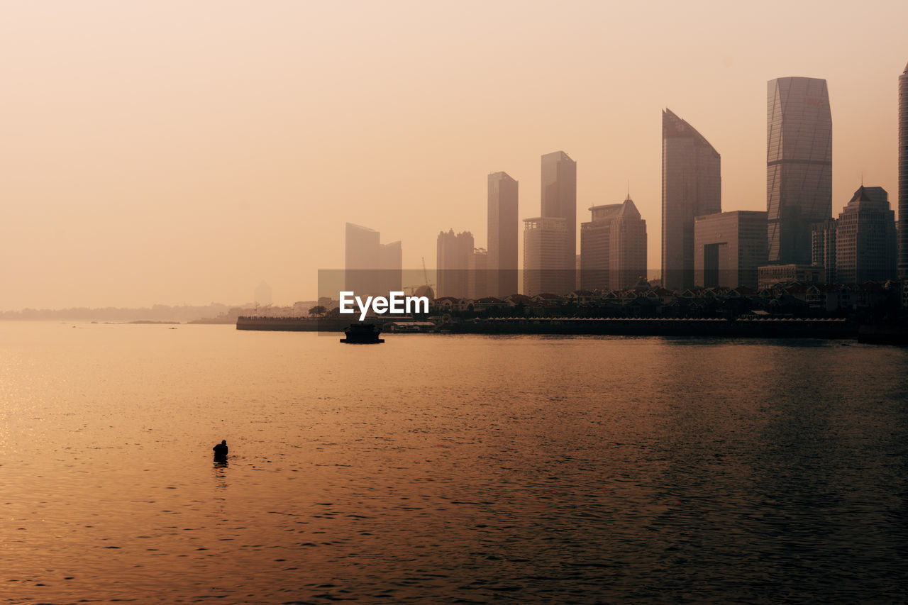 Scenic view of city by sea against sky during sunset