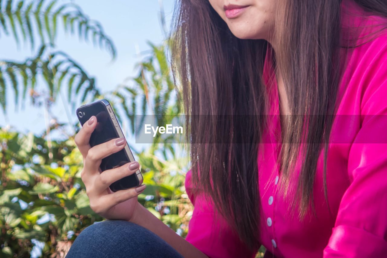 MIDSECTION OF WOMAN USING MOBILE PHONE