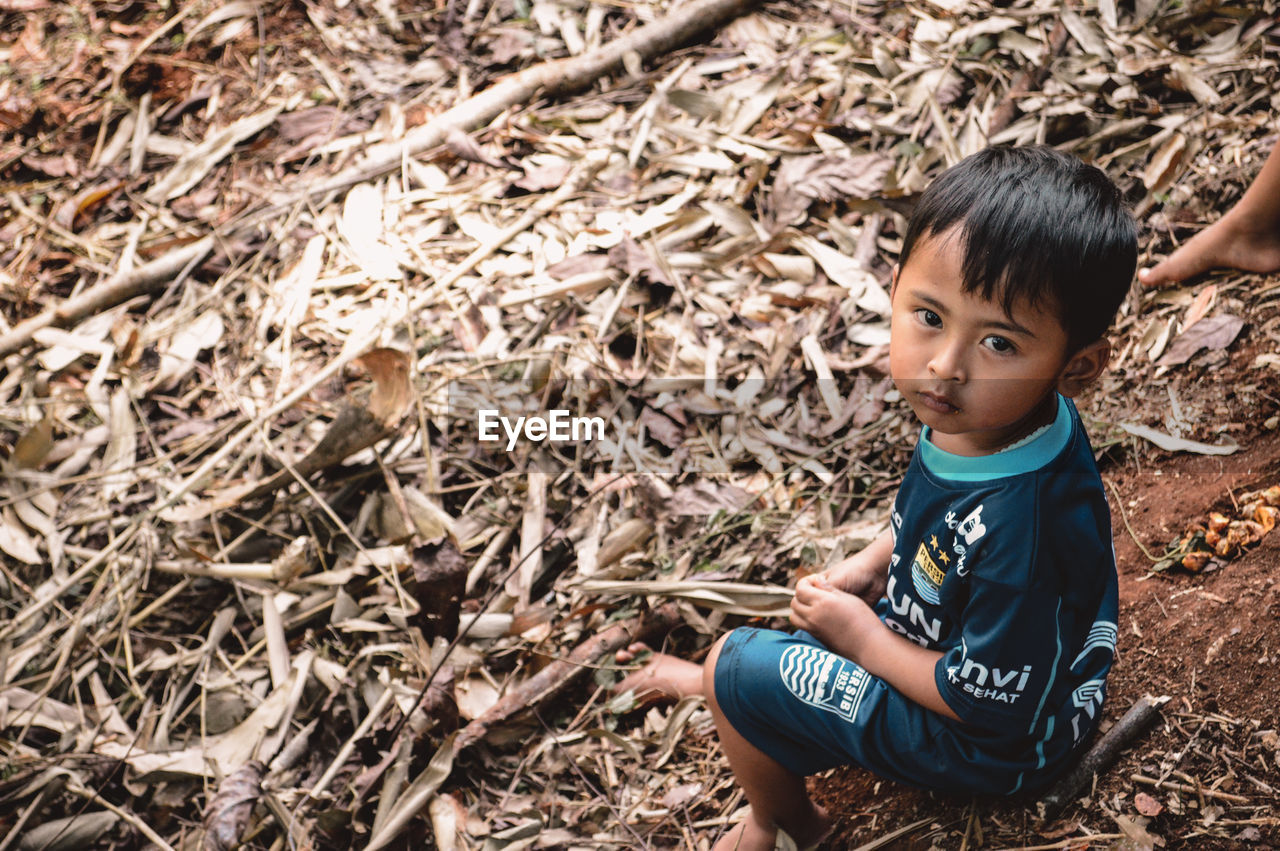 HIGH ANGLE PORTRAIT OF CUTE BOY SITTING ON LAND