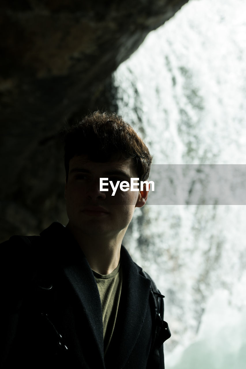 PORTRAIT OF YOUNG MAN STANDING AGAINST CLOUDS
