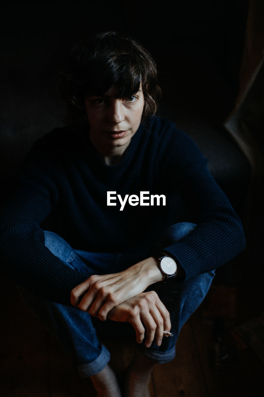 PORTRAIT OF YOUNG MAN SITTING IN DARK