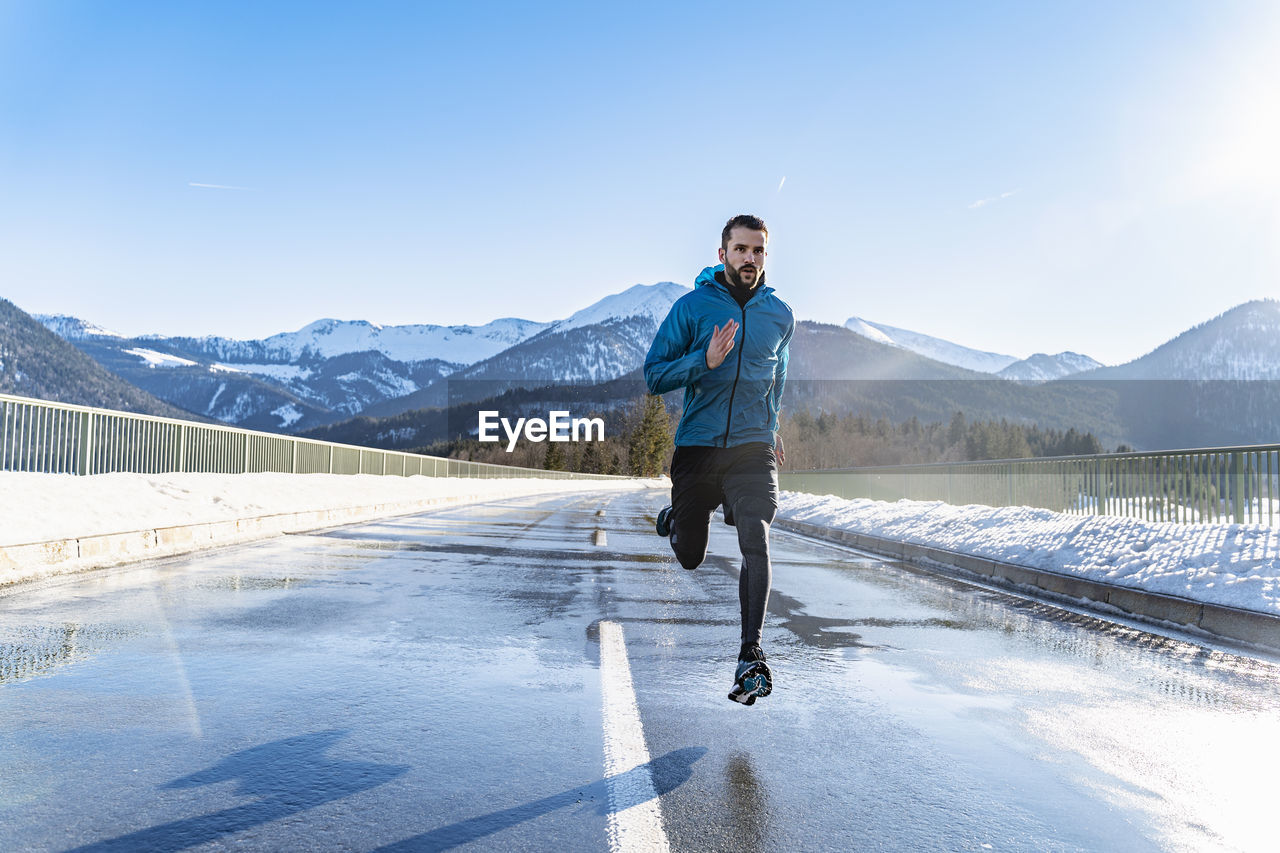 Germany, bavaria, sportive man running on a road in winter