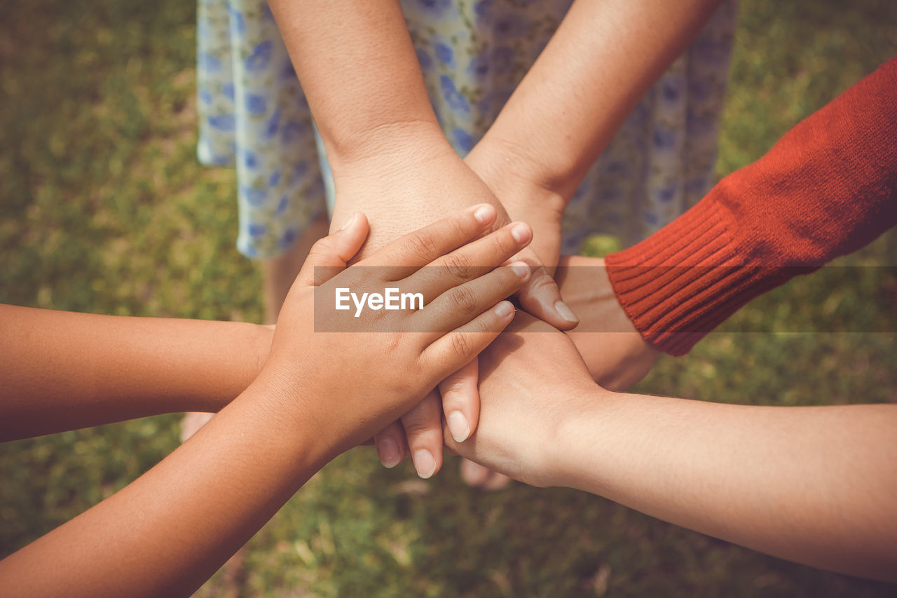 Cropped image of friends stacking hands over grassy field at park