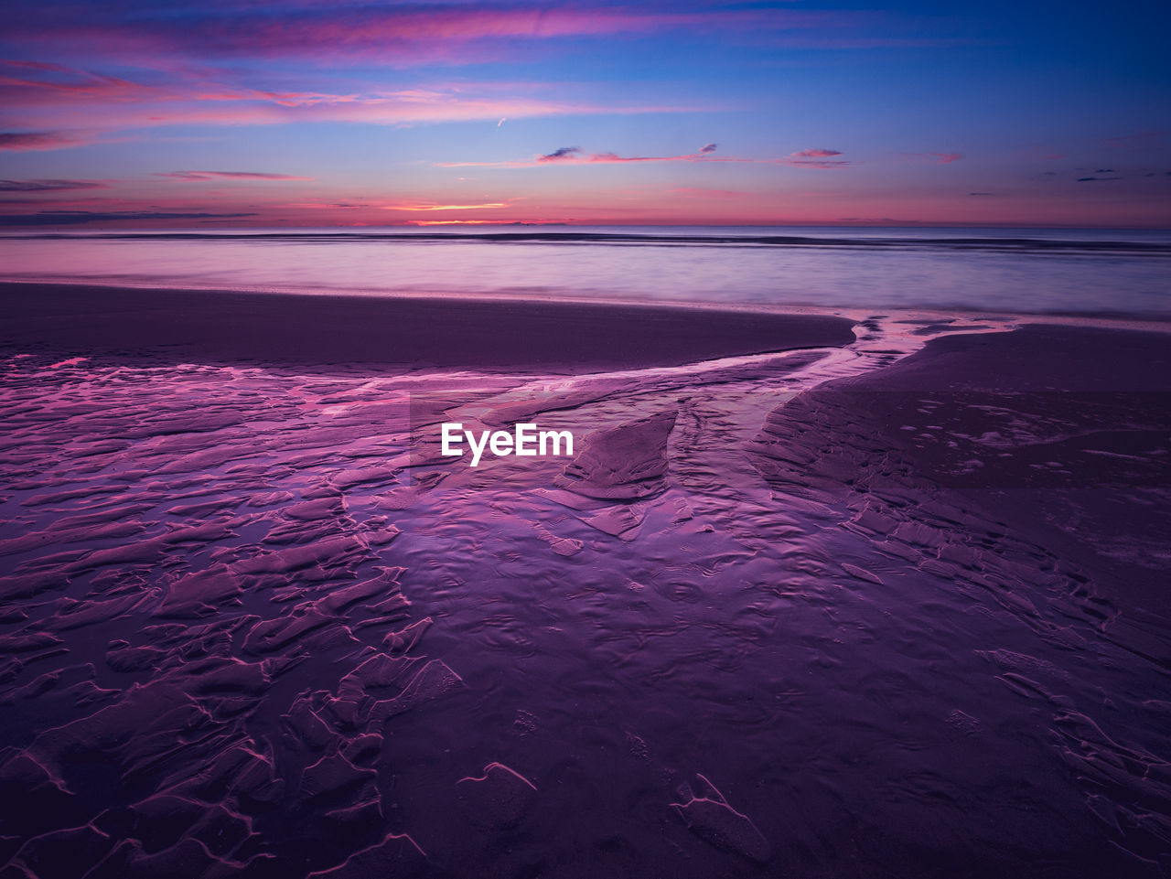 Colorful purple sunset at the beach with sand ripples in the foreground at low tide