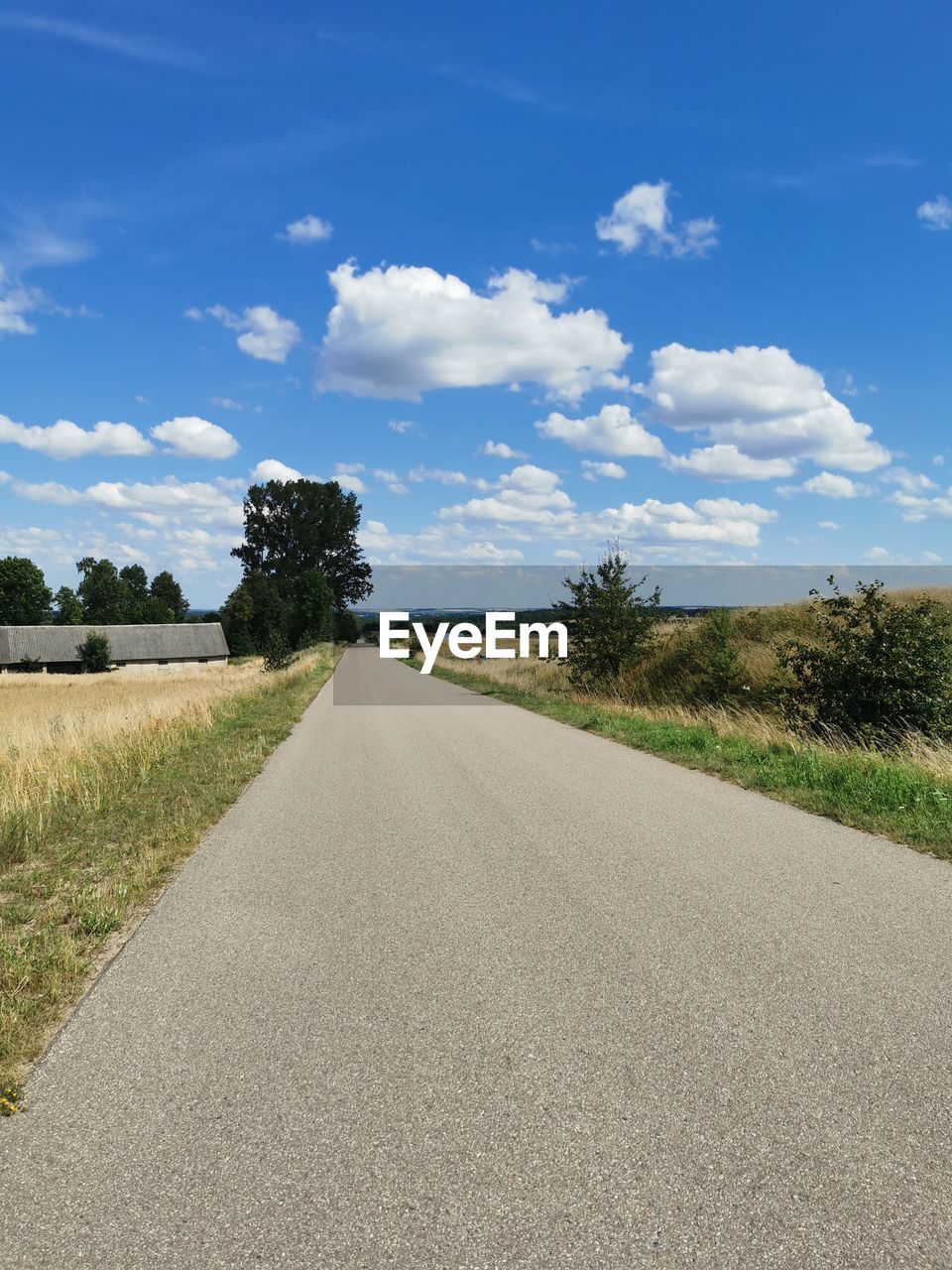 Empty road amidst field against sky