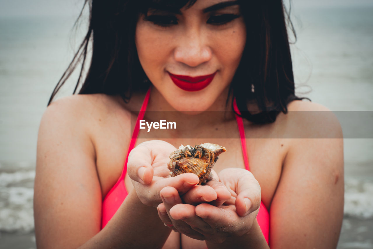 Portrait of woman holding hermit crab at beach