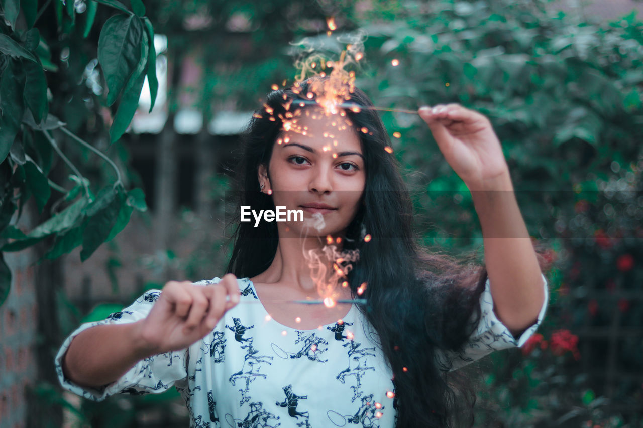 Portrait of girl holding illuminated sparklers against plants