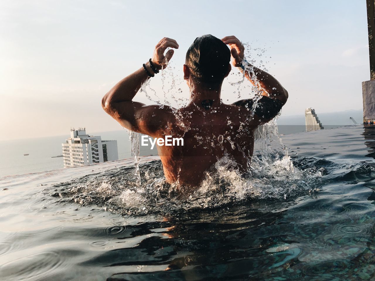 Rear view of shirtless man swimming in infinity pool