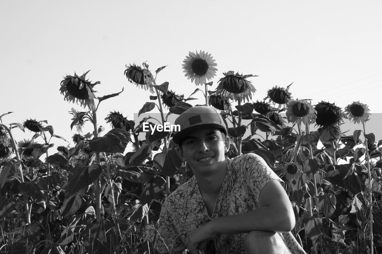 Portrait of teenage boy crouching against sunflowers