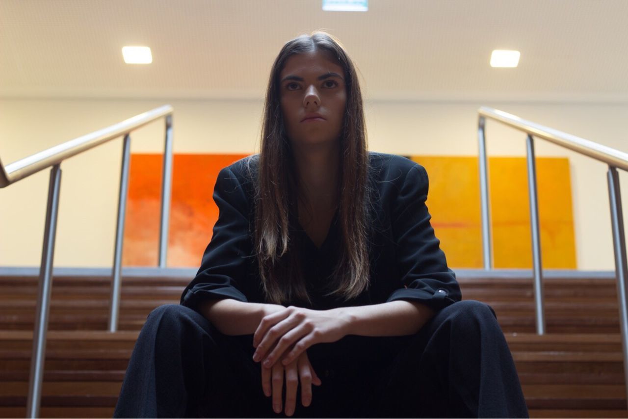 Low angle view of young fashion model sitting on steps against illuminated building