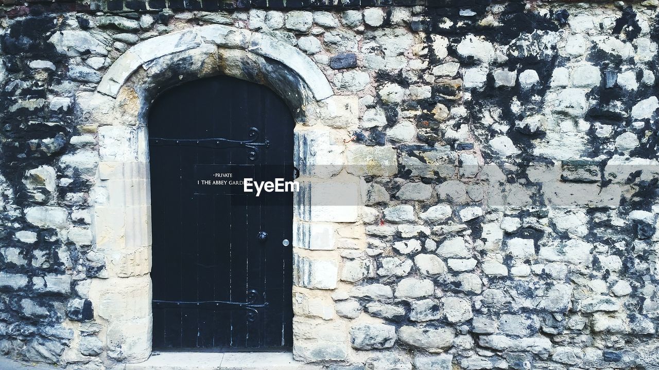 Closed black door of stone wall building with label