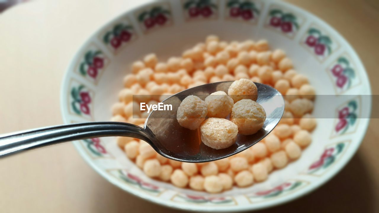 Close-up of cereal in spoon over bowl on table