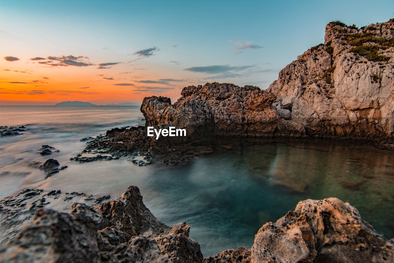 Rock formation on sea shore against sky during sunset