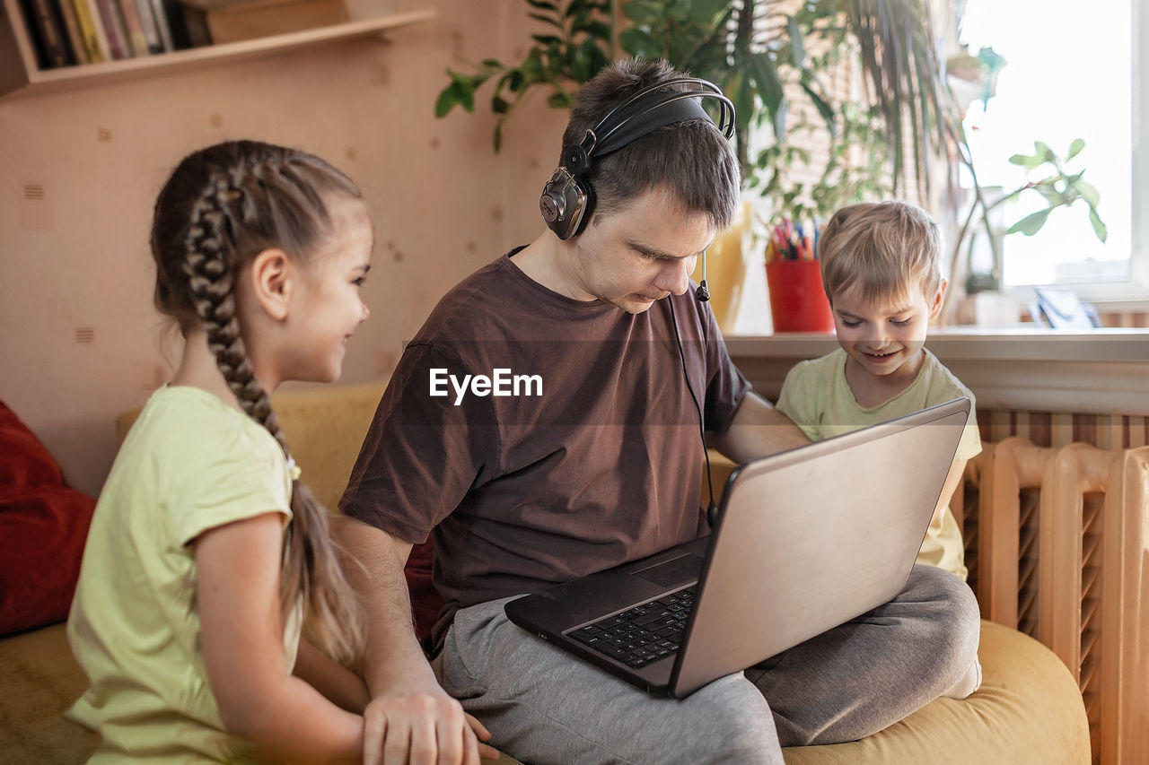 REAR VIEW OF SIBLINGS SITTING ON LAPTOP