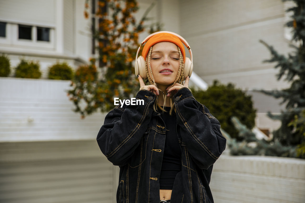 Fashionable woman with eyes closed listening music through headphones in front yard