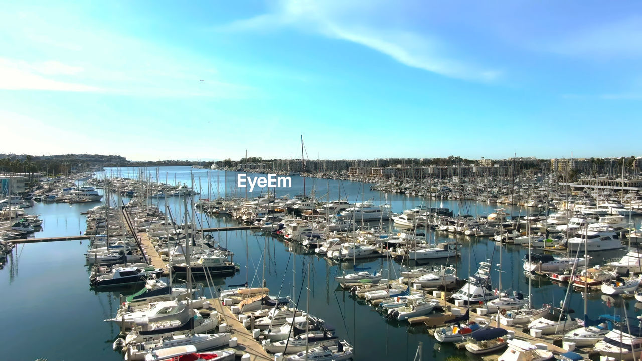 water, nautical vessel, marina, transportation, harbor, sky, architecture, dock, mode of transportation, cityscape, sea, port, moored, nature, city, building exterior, ship, no people, built structure, cloud, pier, day, high angle view, travel destinations, sailboat, building, outdoors, aerial photography, travel, boat, vehicle, commercial dock, sunlight, blue, infrastructure, yacht