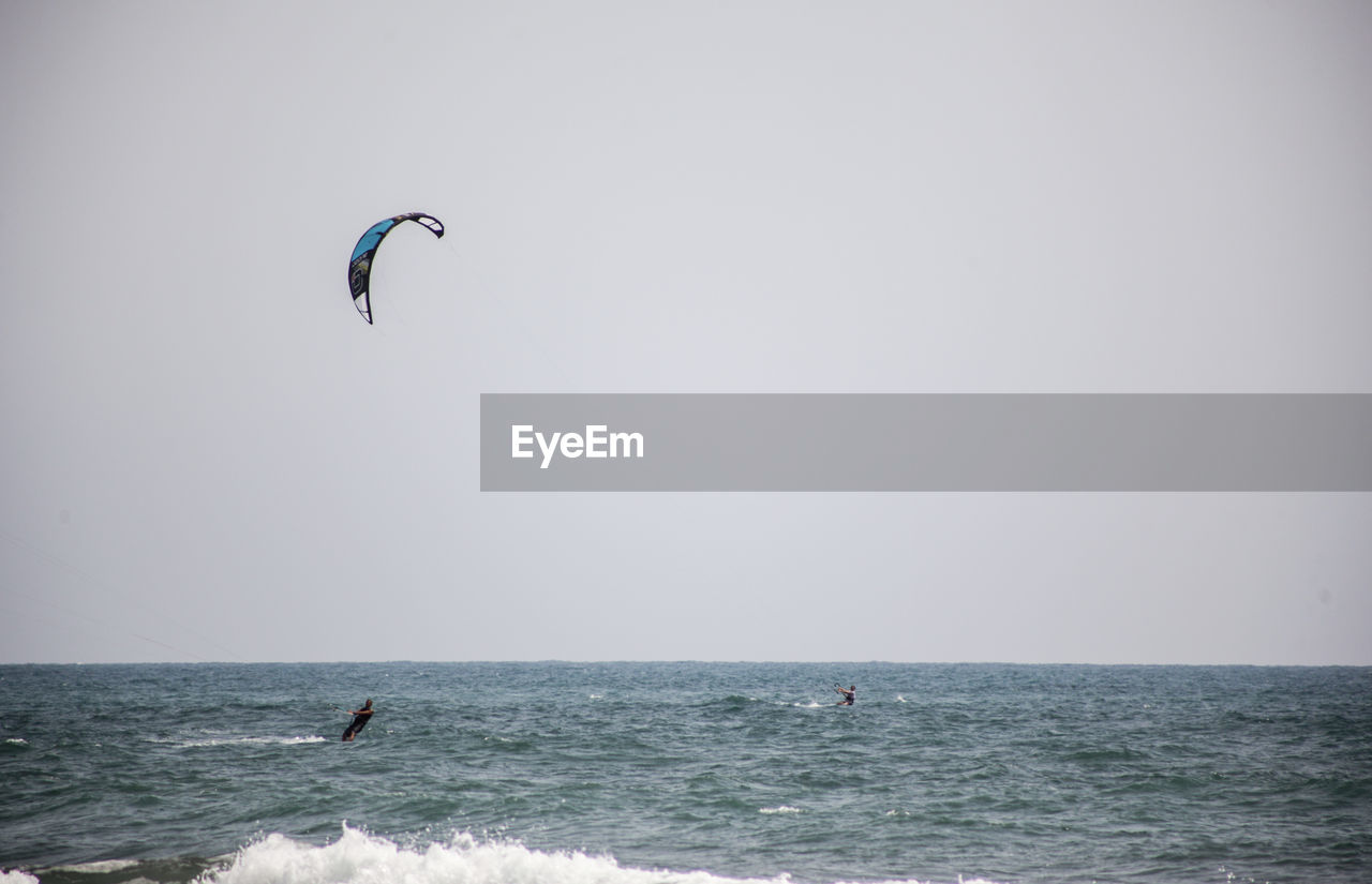 Men kitesurfing in sea against clear sky