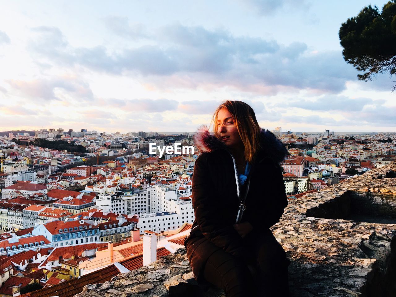 Woman looking at cityscape against cloudy sky during sunset