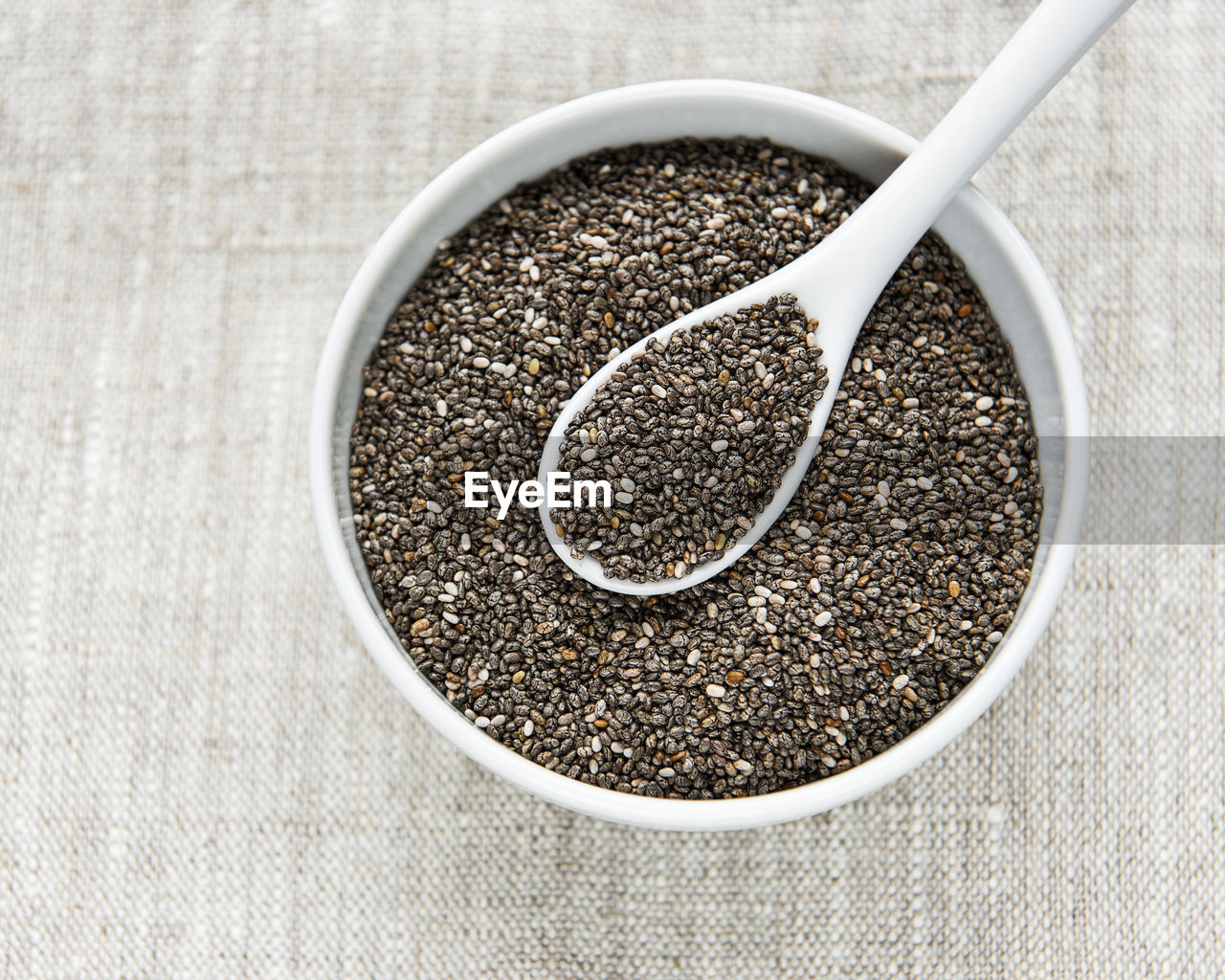 Chia seeds in white bowl and spoon on textile background.