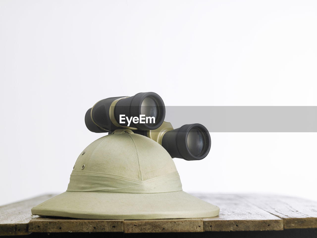 Close-up of hat with binoculars on table against white background