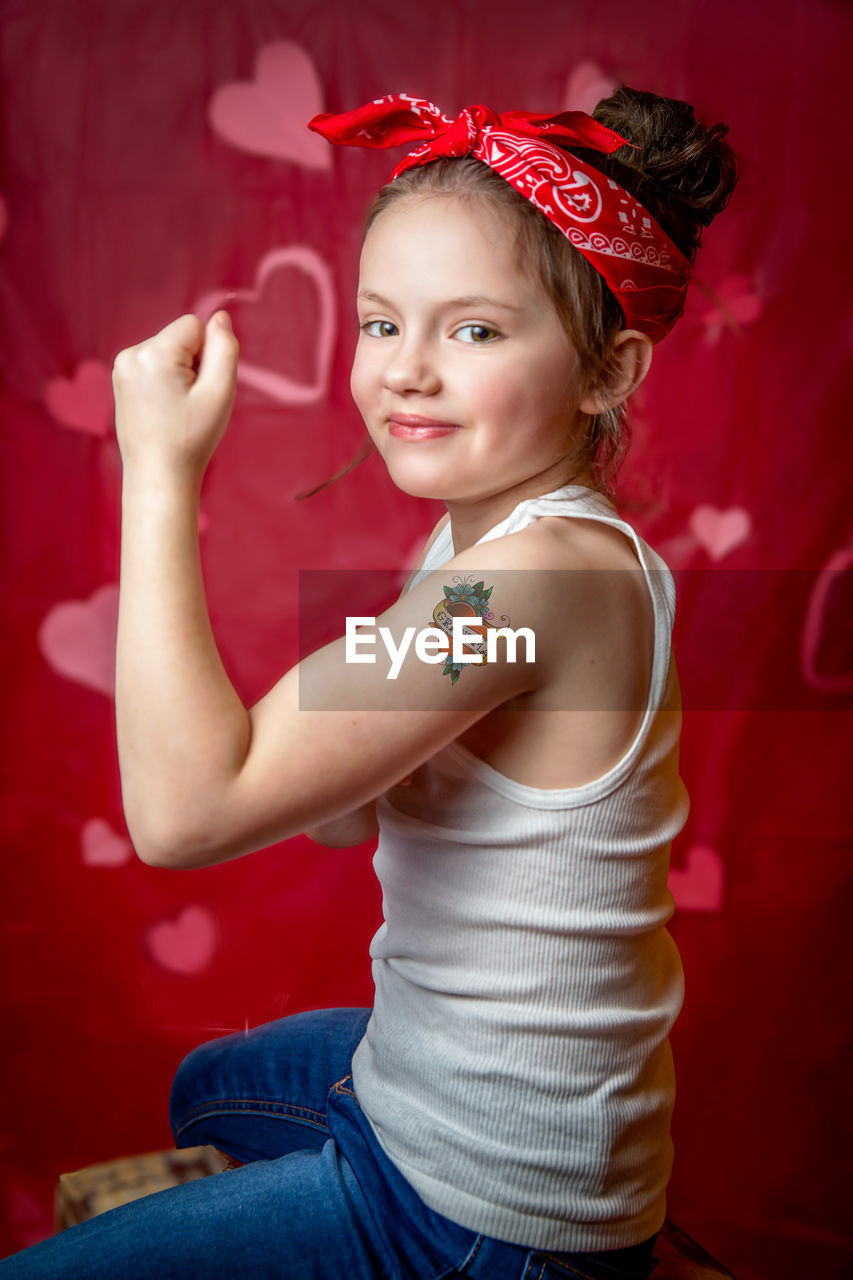 Portrait of smiling girl showing tattoo against red background