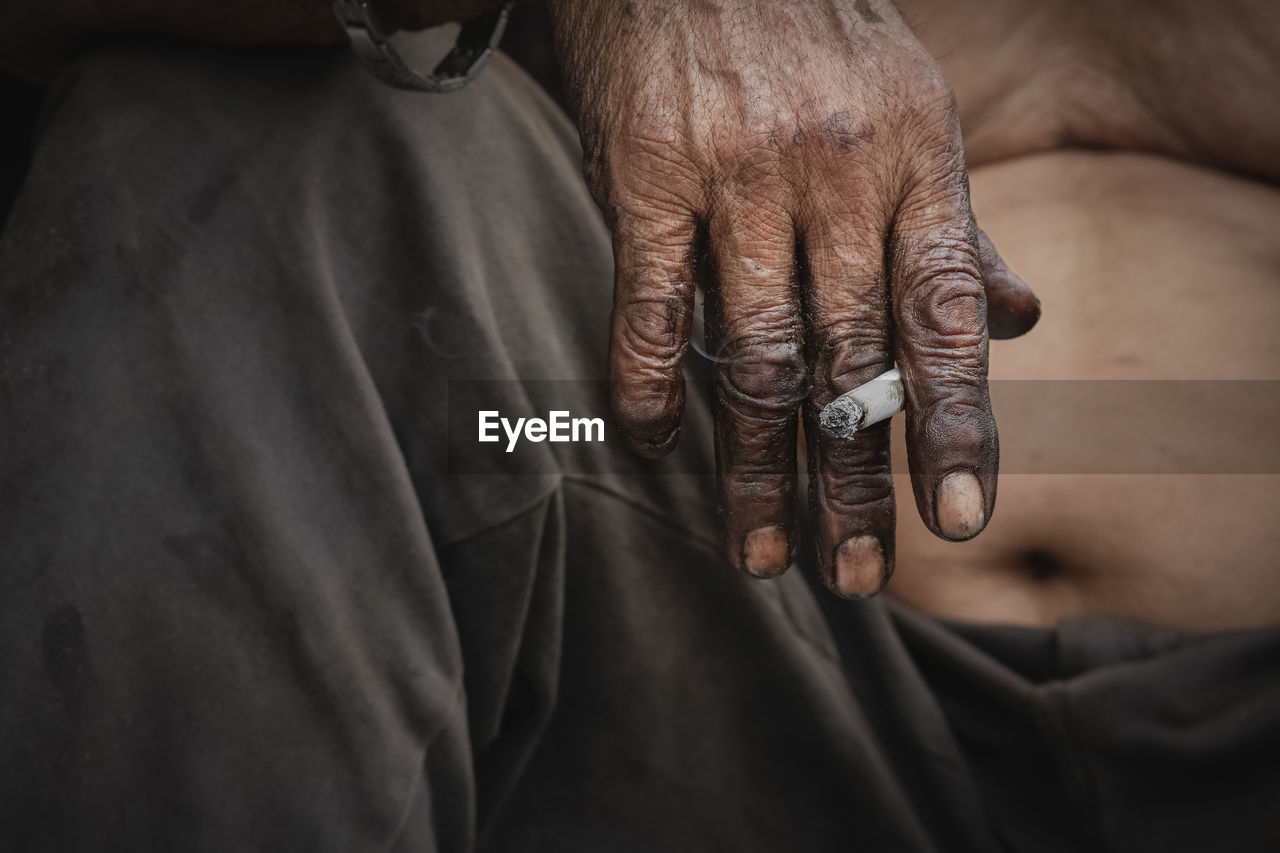 Midsection of shirtless man holding cigarette