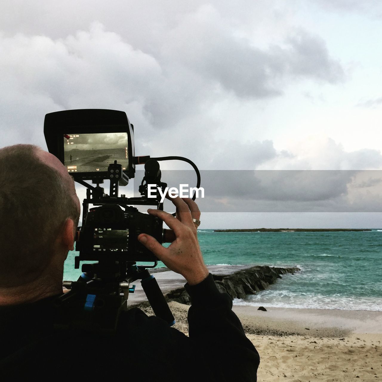 Rear view of man photographing at beach against sky