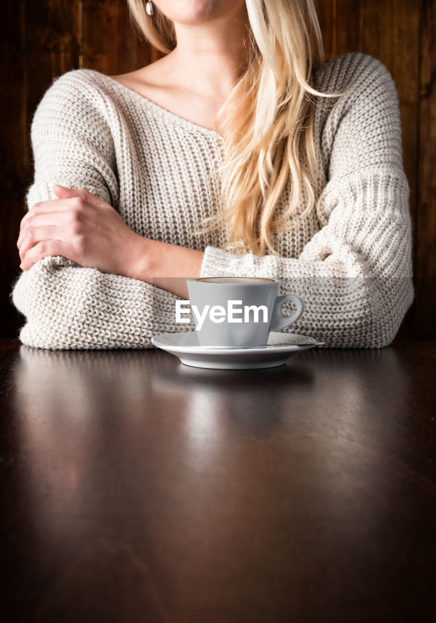 Midsection of woman drinking coffee on a wooden table