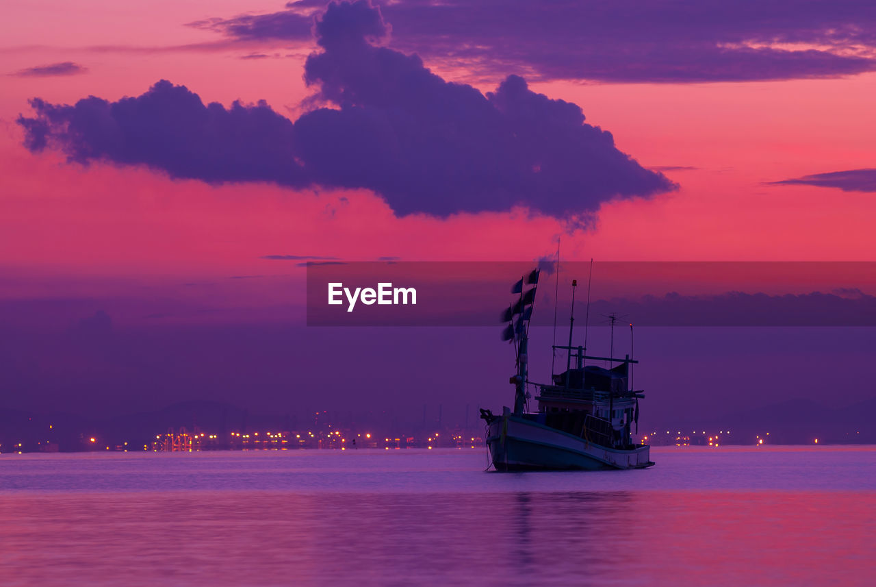 Sailboat sailing in sea against dramatic sky during sunset