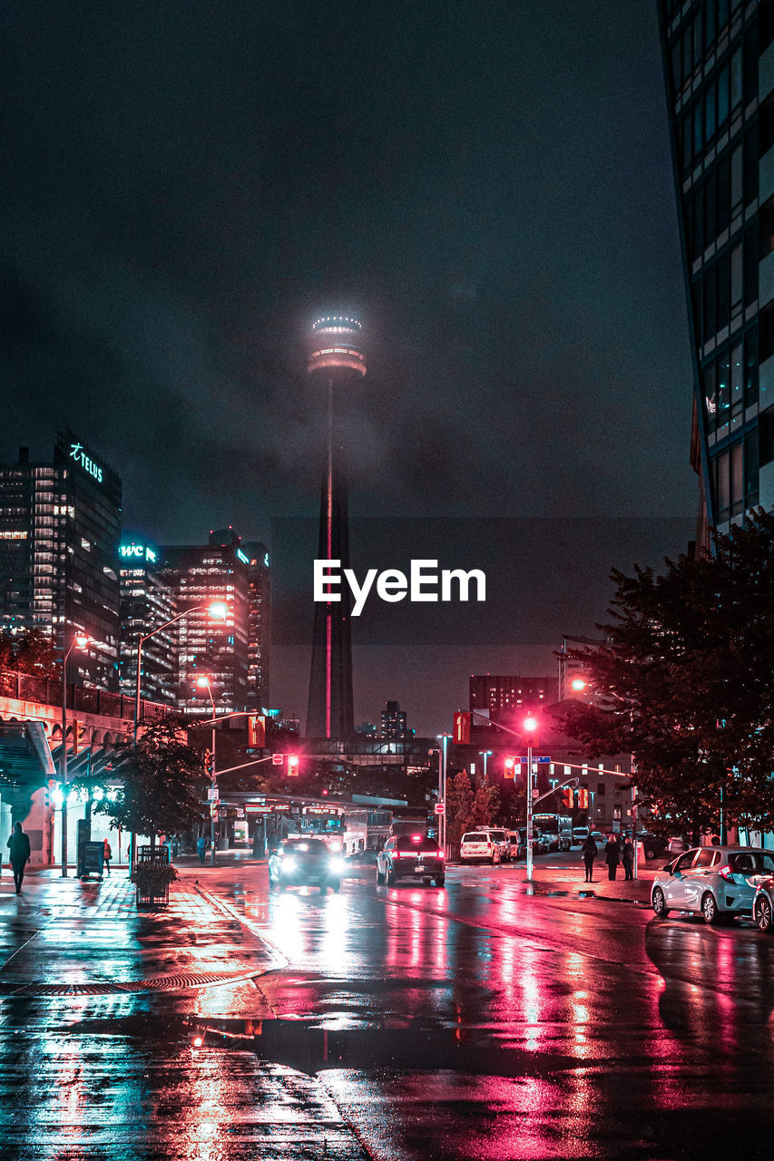Illuminated buildings by street against sky at night