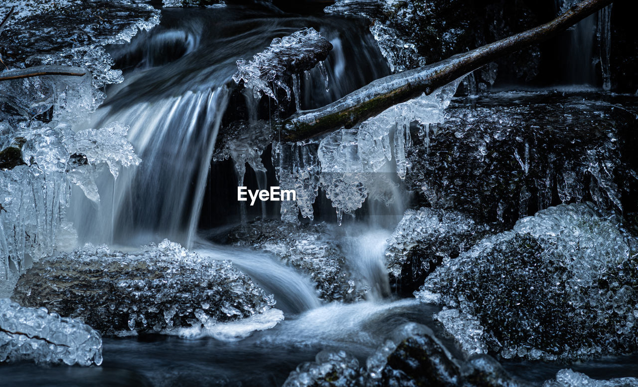 Detail of smell waterfall in a forest creek with frozen rocks and icicles.