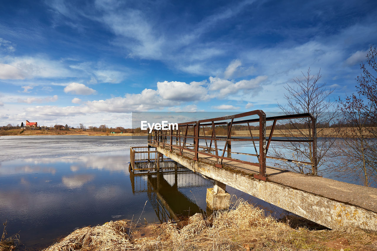 water, sky, reflection, cloud, nature, shore, river, architecture, built structure, landscape, environment, scenics - nature, no people, morning, coast, land, blue, tranquility, bridge, outdoors, reservoir, beauty in nature, day, wood, travel destinations, plant, beach, tranquil scene, travel, horizon, tree, waterway, transportation, non-urban scene, rural scene