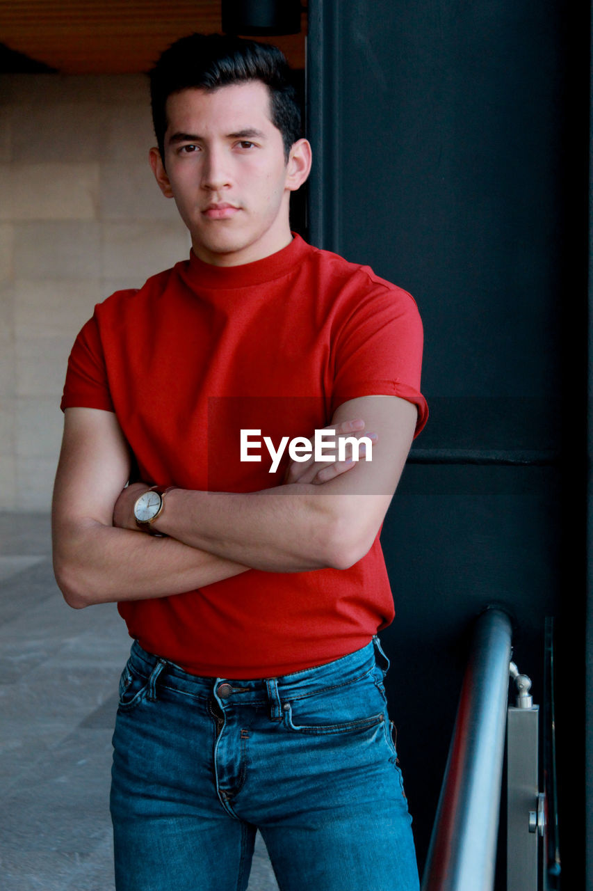 Portrait of young man with arms crossed standing in corridor