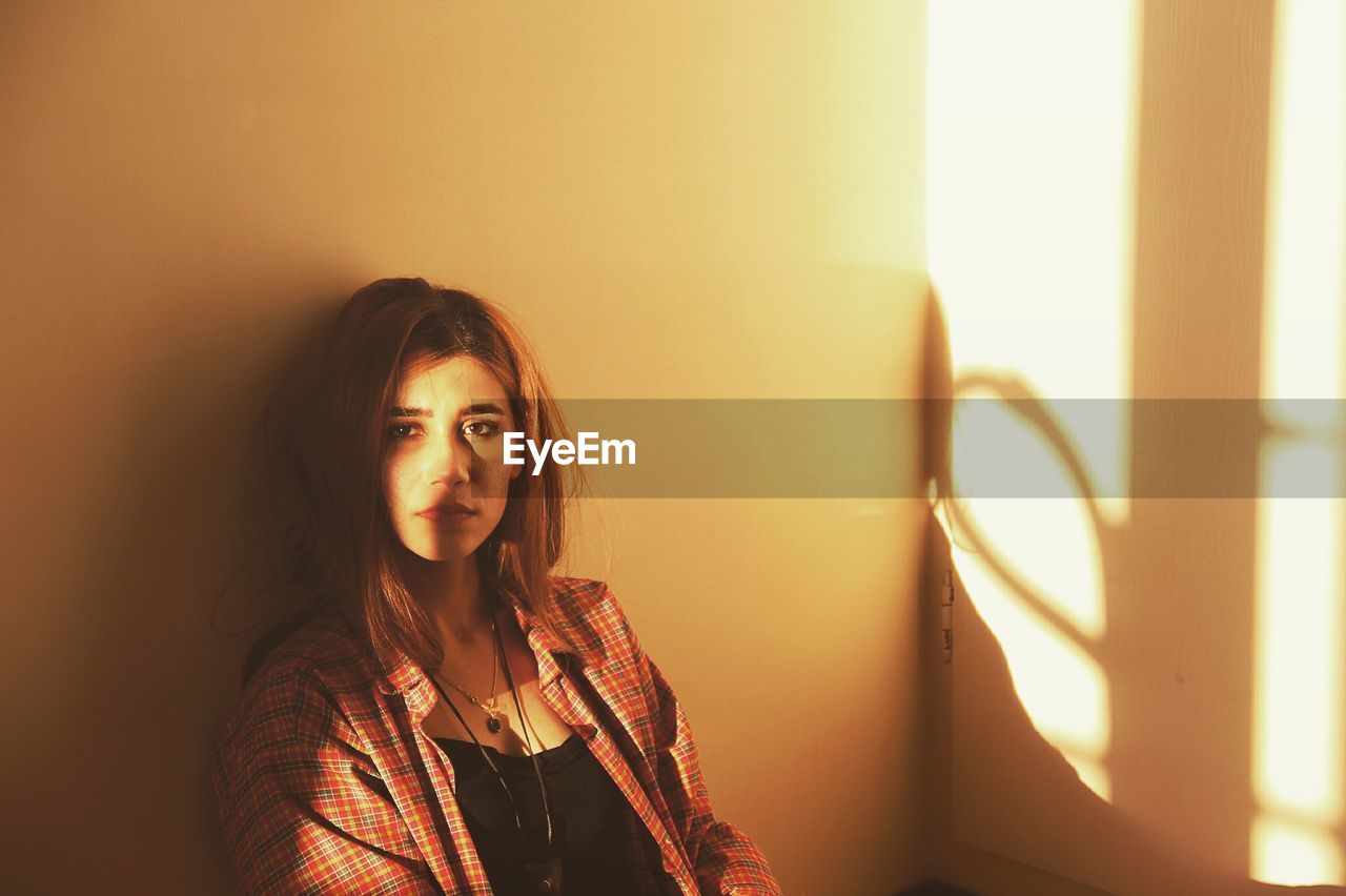 PORTRAIT OF BEAUTIFUL YOUNG WOMAN LOOKING AWAY AGAINST WALL AT HOME