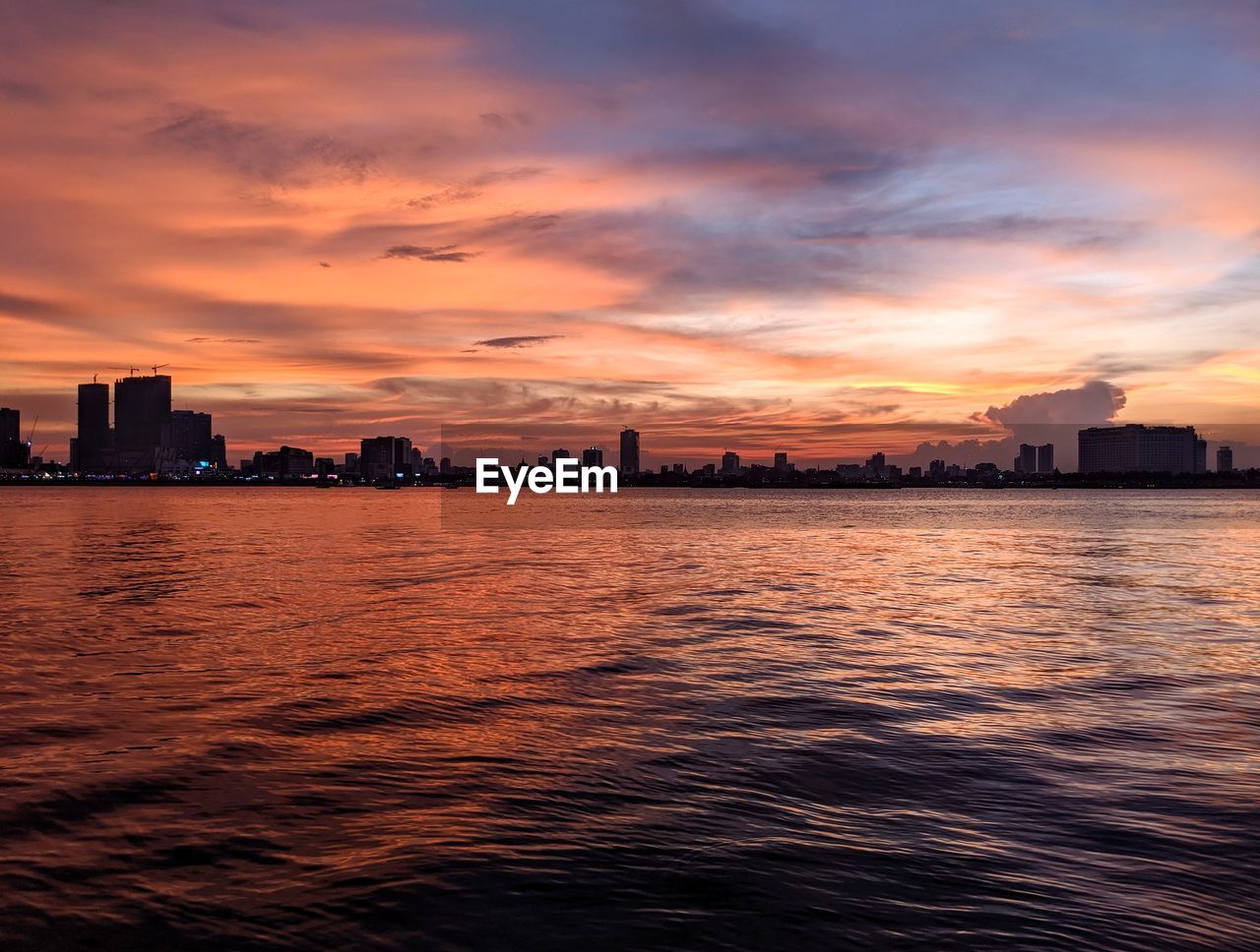 Sea by buildings against sky during sunset