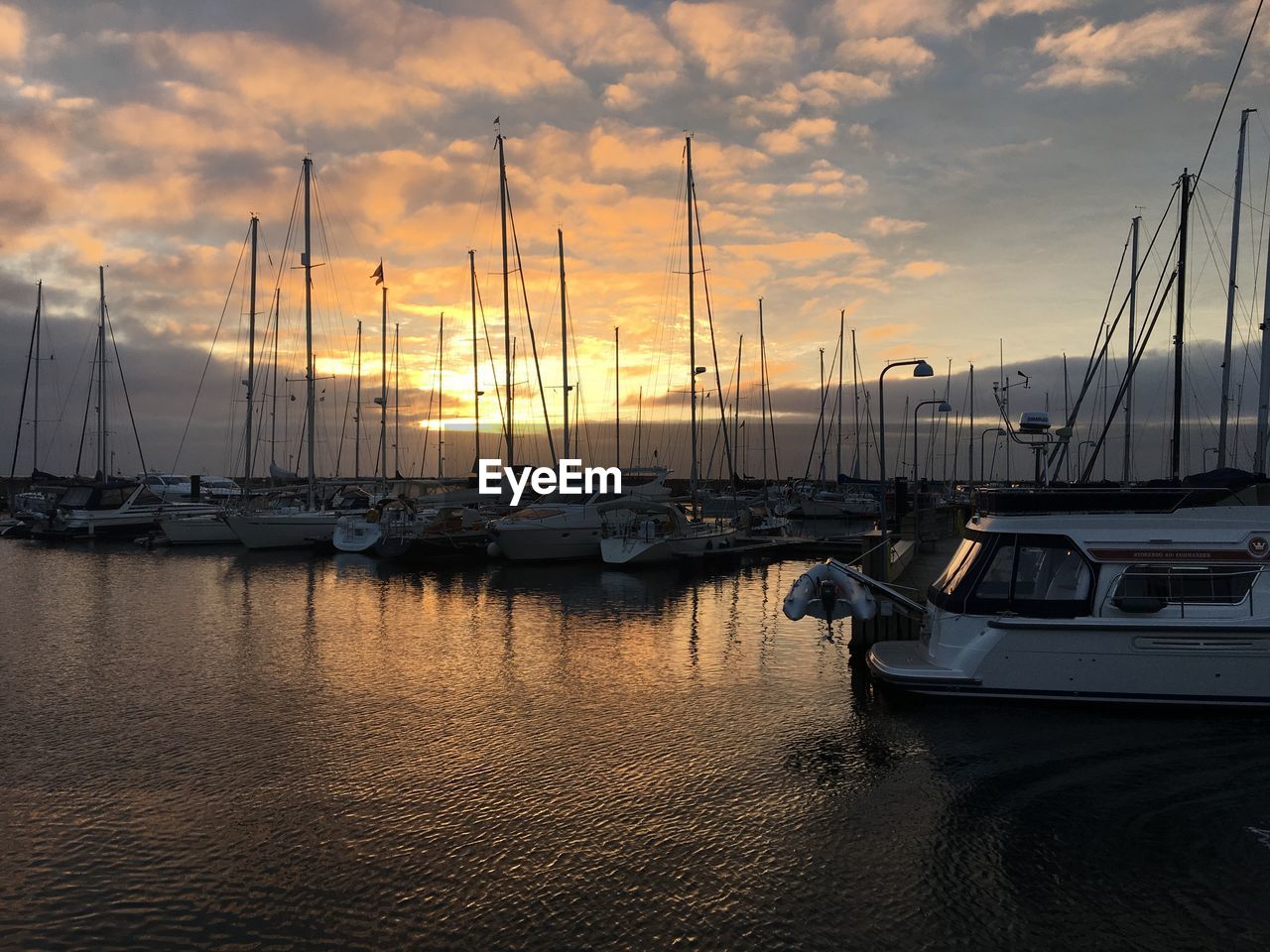 Sailboats moored on harbor against sky during sunset