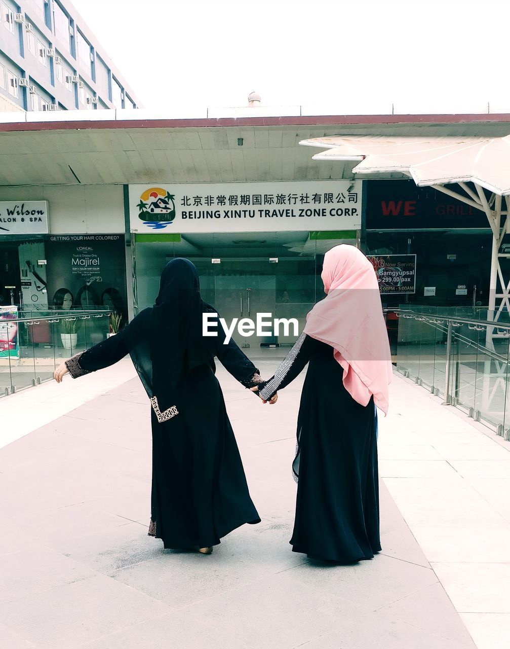 Women in burka holding hands against building