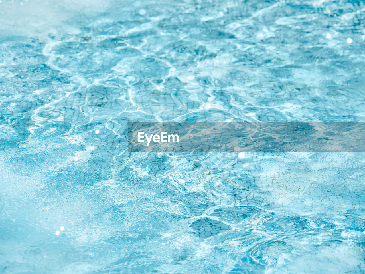 Sun beams on surface of water in fountain with blue mosaic bottom.  pattern of transparent water.