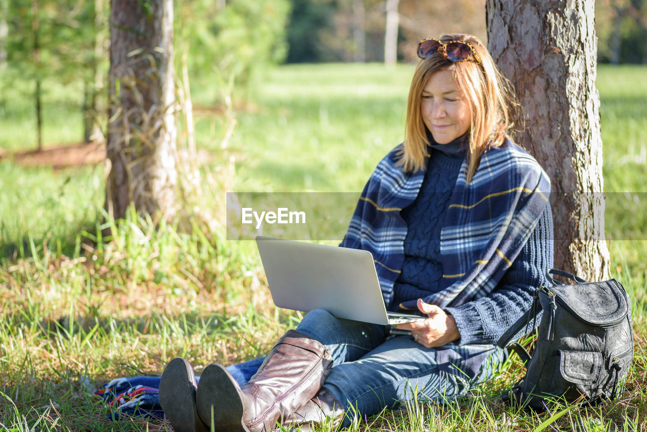 Mature woman using laptop while sitting on field in park