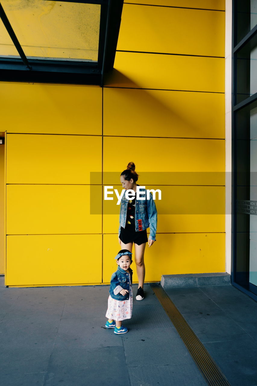 Mother with cute daughter standing against building