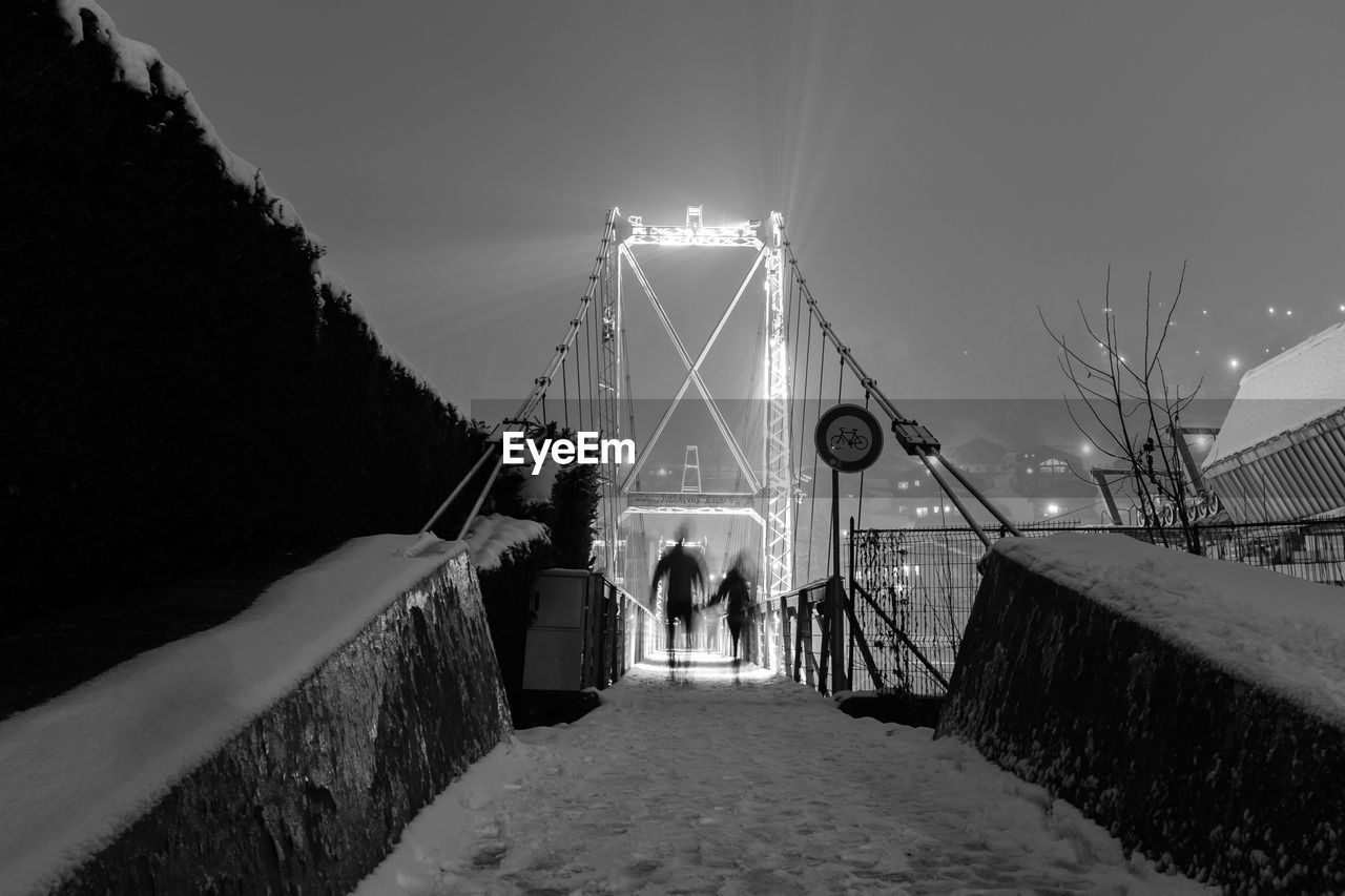 Rear view of people on illuminated bridge at night