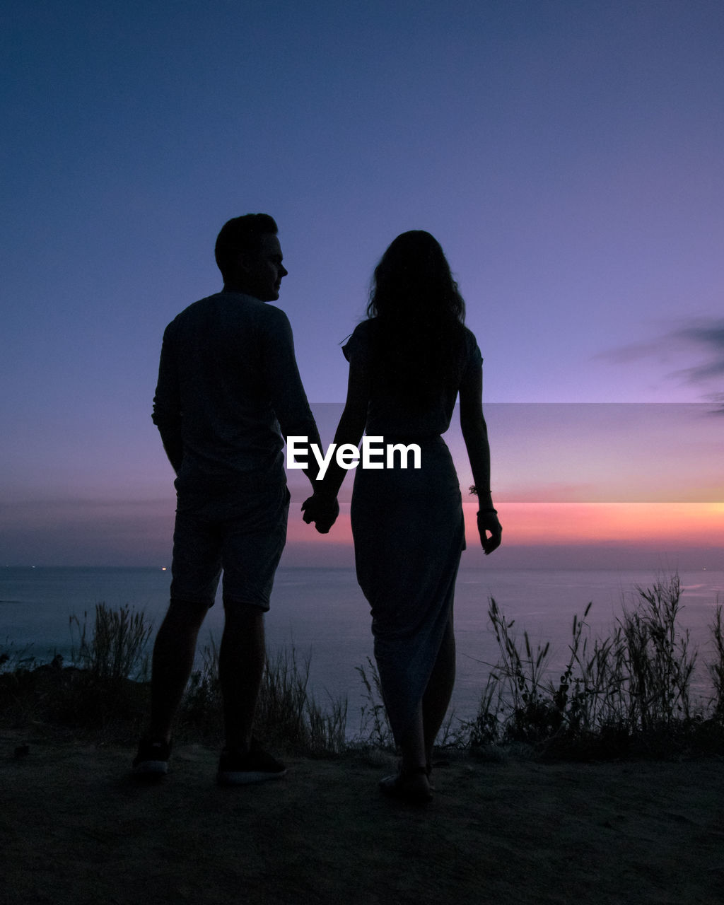 Silhouette couple holding hands while standing against sky during sunset