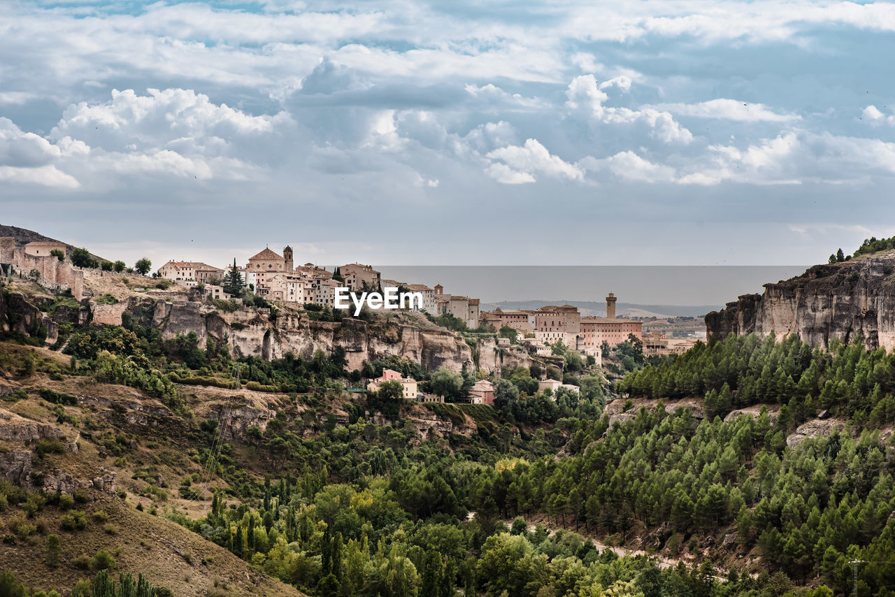 Scenic view of medieval town cuenca with old stone houses located on hills covered with green trees under blue cloudy sky in summer day in spain