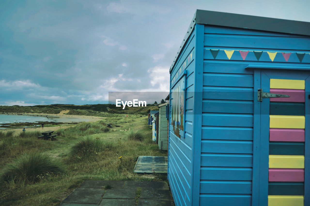 sky, cloud, nature, architecture, land, no people, landscape, built structure, blue, hut, day, beach, grass, plant, outdoors, building exterior, shed, scenics - nature, transport, environment, rural scene, transportation, tranquility, multi colored, building, travel destinations, beach hut, wood