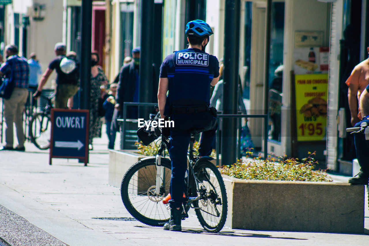 REAR VIEW OF MAN CYCLING ON STREET