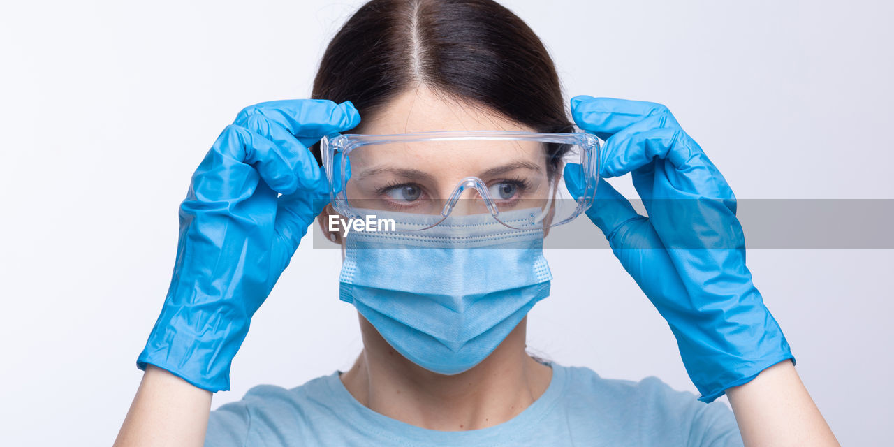 Doctor in mask wearing surgical glove looking away against gray background