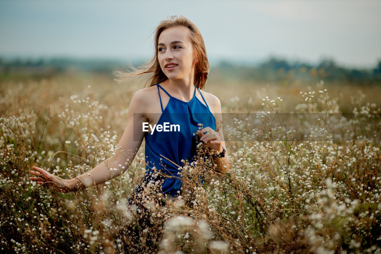 PORTRAIT OF SMILING YOUNG WOMAN ON FIELD