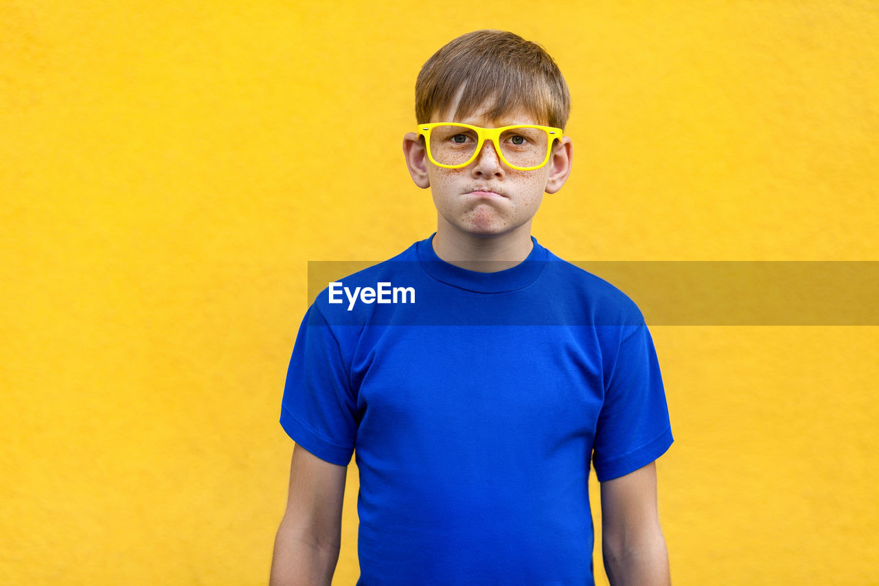 Portrait of boy standing against yellow background