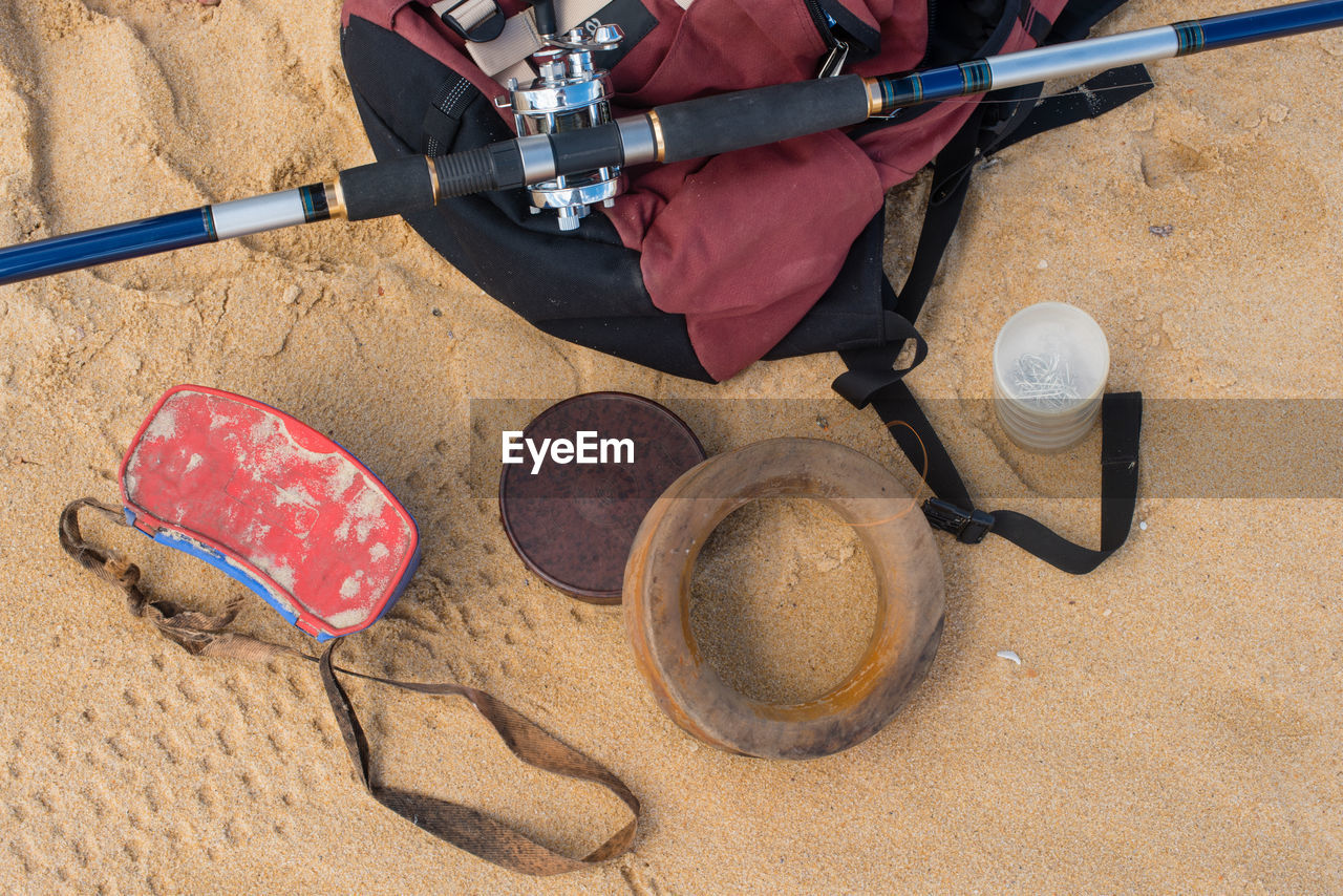 High angle view of backpack with fishing rod on sand at beach